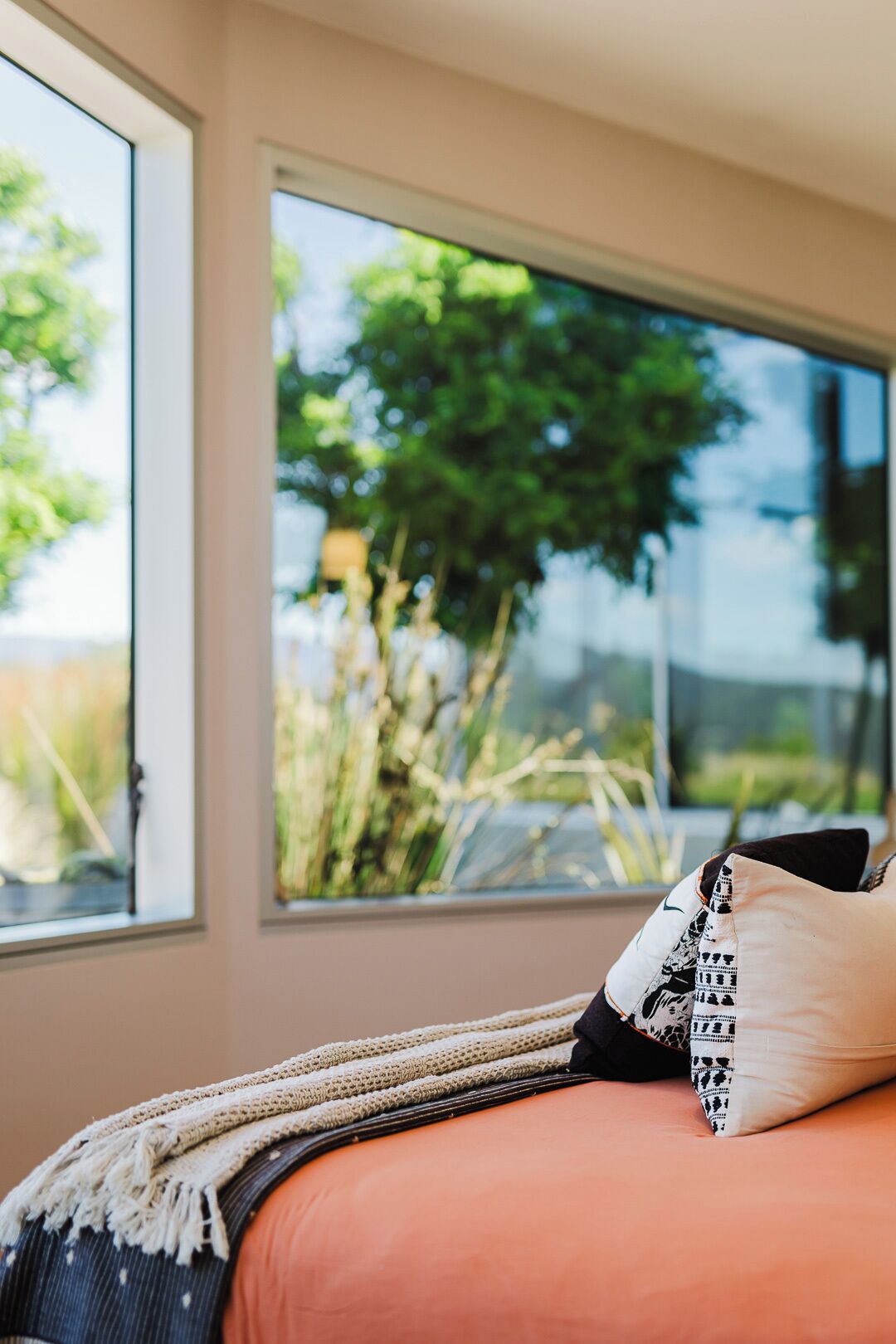 A room with a large window, a bed with a patterned pillow, and a knitted throw.