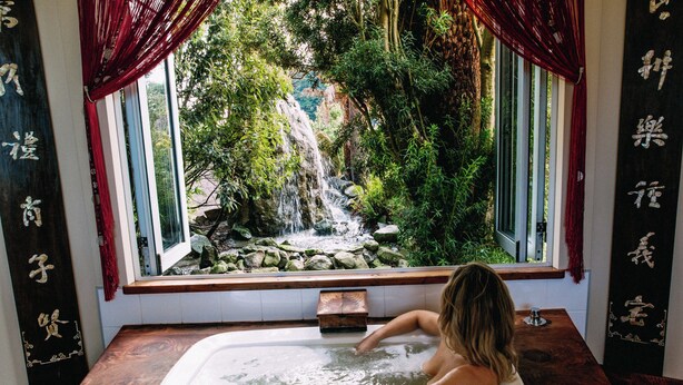 Una bañera con vistas a una cascada y vegetación.