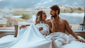 Una pareja en la cama con vistas a la montaña a través de una ventana.