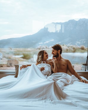 A couple in bed with a mountain view through a window.
