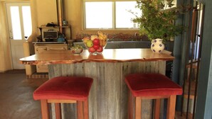 A kitchen with a wooden island, two red cushioned stools, a fruit bowl, and a potted plant. - Timbarra Hideaway - the perfect retreat (Buchan)