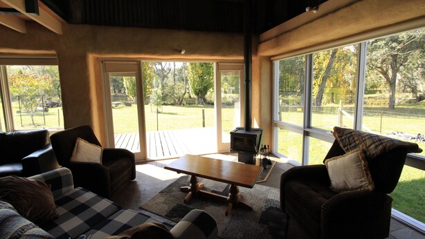 A cozy living room with a fireplace, large windows, and a checkered sofa. - Timbarra Hideaway - the perfect retreat (Buchan)