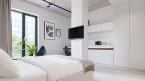 Een moderne slaapkamer met een groot bed, een televisie en een minimalistische keukenhoek.