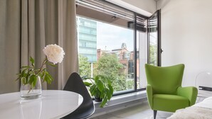 Een moderne kamer met een groot raam, een groene fauteuil, een witte tafel en een potplant.