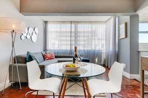 Ein modernes Wohnzimmer mit einem Glastisch, weißen Stühlen, einem grauen Sofa und einer Stehlampe.