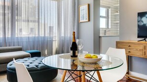 A modern living room with a glass table, a sofa, and a TV. - Backup-Power Perfect Modern Beach Apartment near V&A with Sea and Park Views (Cape Town)