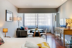 A modern hotel room with a bed, a dining table, a sofa, and a TV.