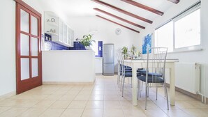 Un'ampia cucina con zona pranzo, caratterizzata da un pavimento in piastrelle bianche, una porta in legno e una finestra che lascia entrare luce naturale.