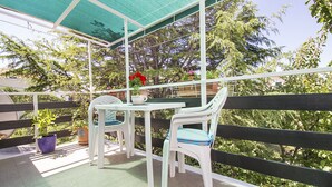 Patio esterno con tavolo e due sedie, circondato da un recinto in legno e vegetazione.