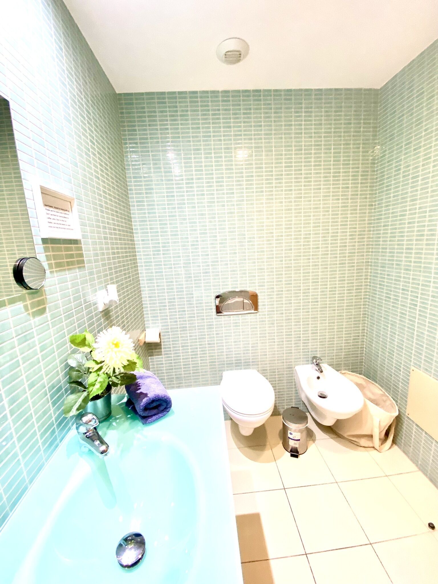 Un baño con bañera, inodoro y bidé. Las paredes están cubiertas de un diseño verde.