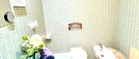 A bathroom with a bathtub, toilet, and bidet. The walls are tiled with a green pattern.