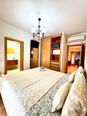 A bedroom with a bed, a chandelier, a wardrobe, and a bathroom visible through an open door.