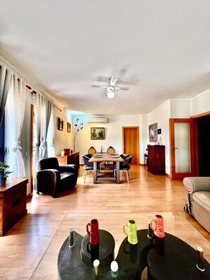 A spacious living room with a dining table, chairs, a ceiling fan, and a sofa.