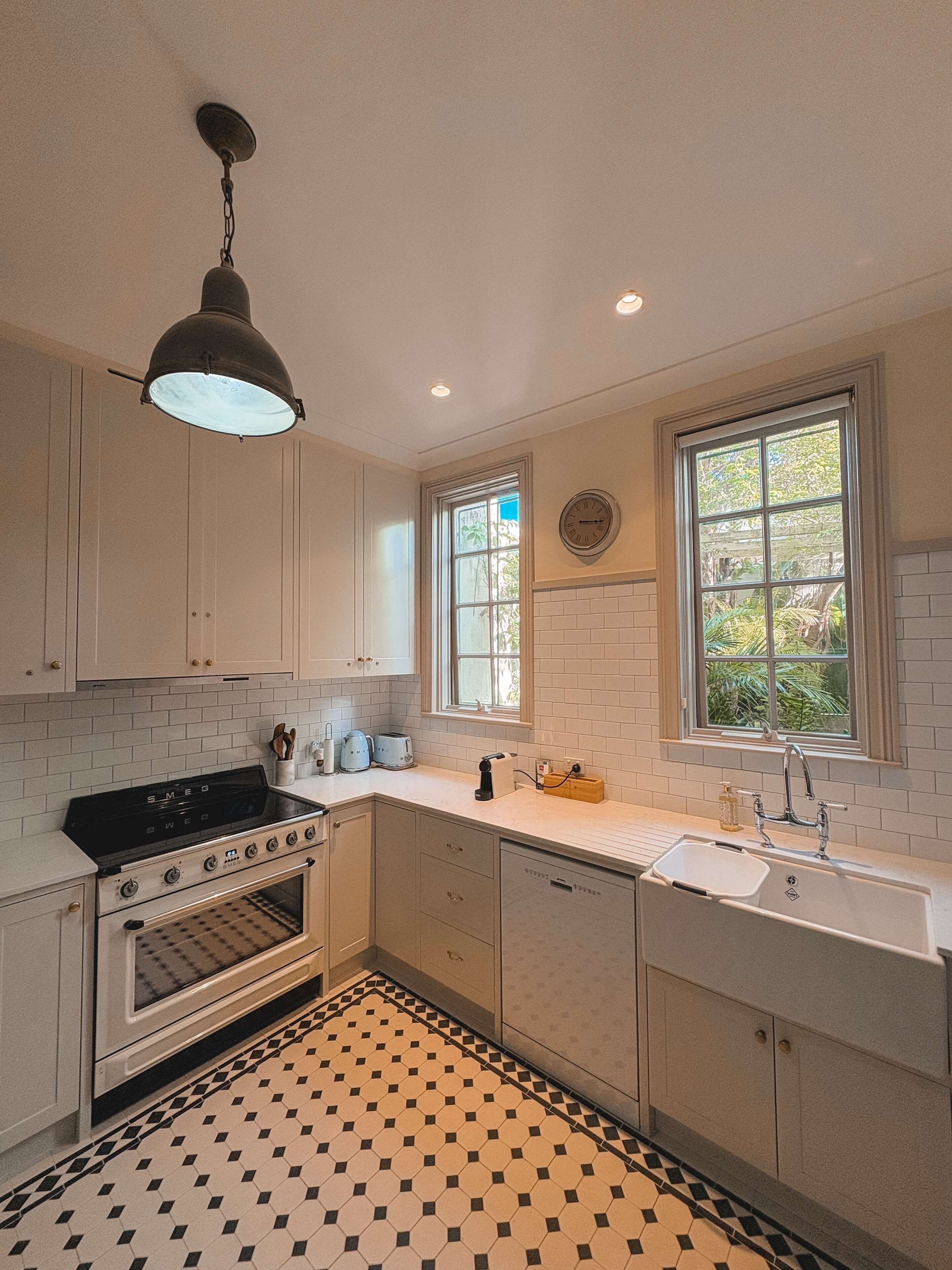 A kitchen with white cabinets, a black stove, a tiled floor, and a window with a view of greenery.