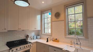 A kitchen with white cabinets, a black stove, a tiled floor, and a window with a view of greenery.