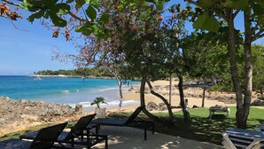 A beachside patio with lounge chairs and a table, overlooking a sandy beach and the ocean.