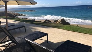 A beachside patio with lounge chairs and a table, overlooking the ocean with waves crashing against rocks.