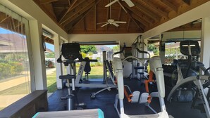 A covered gym area with exercise equipment, including treadmills and weight machines, and a bench with stacked mats. - Jamaica Escape 2 Bedroom  Modern Apt. near beaches attractions & restaurants (Ocho Rios)