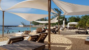 A beach with wooden lounge chairs and tables under white canopies, a wooden fence, and a clear view of the sea. - Jamaica Escape 2 Bedroom  Modern Apt. near beaches attractions & restaurants (Ocho Rios)