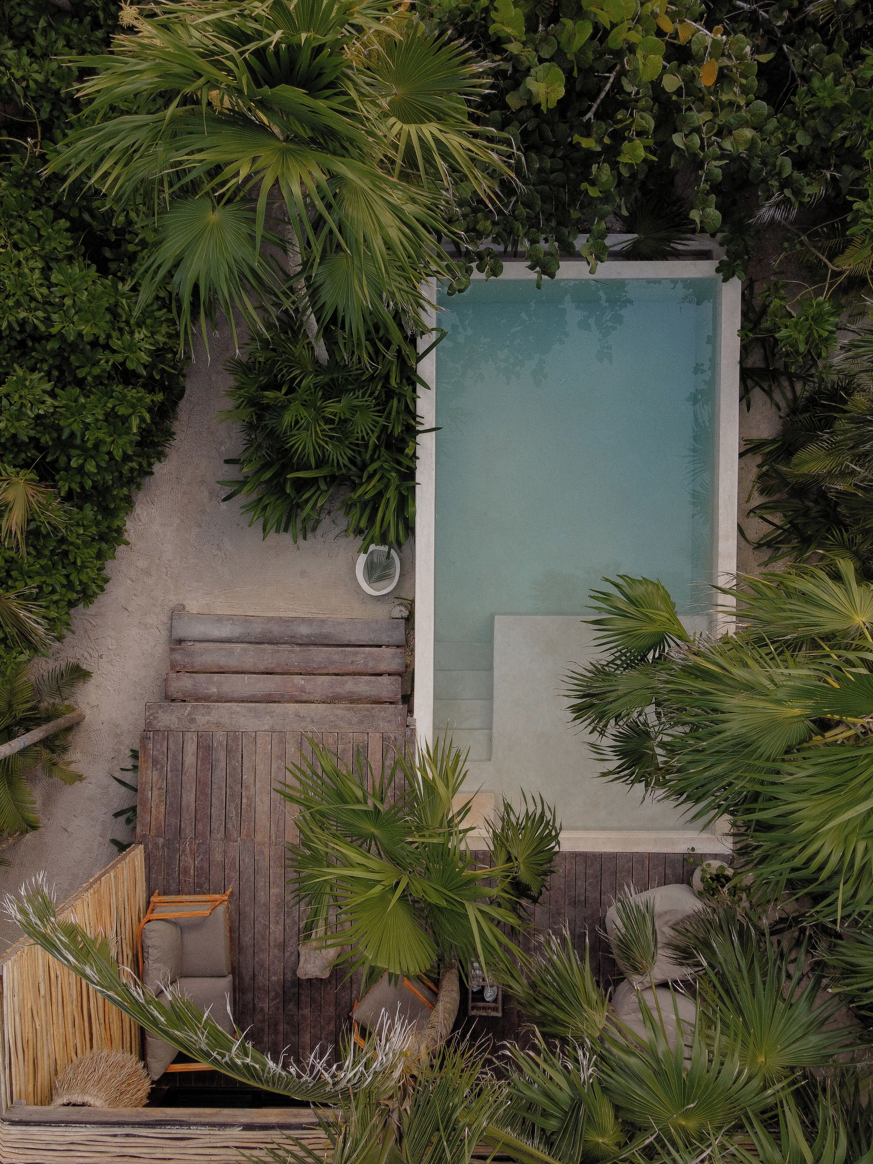 Eine Vogelperspektive auf einen privaten Pool, umgeben von üppiger Vegetation, einer Holzterrasse und einer Hängematte.