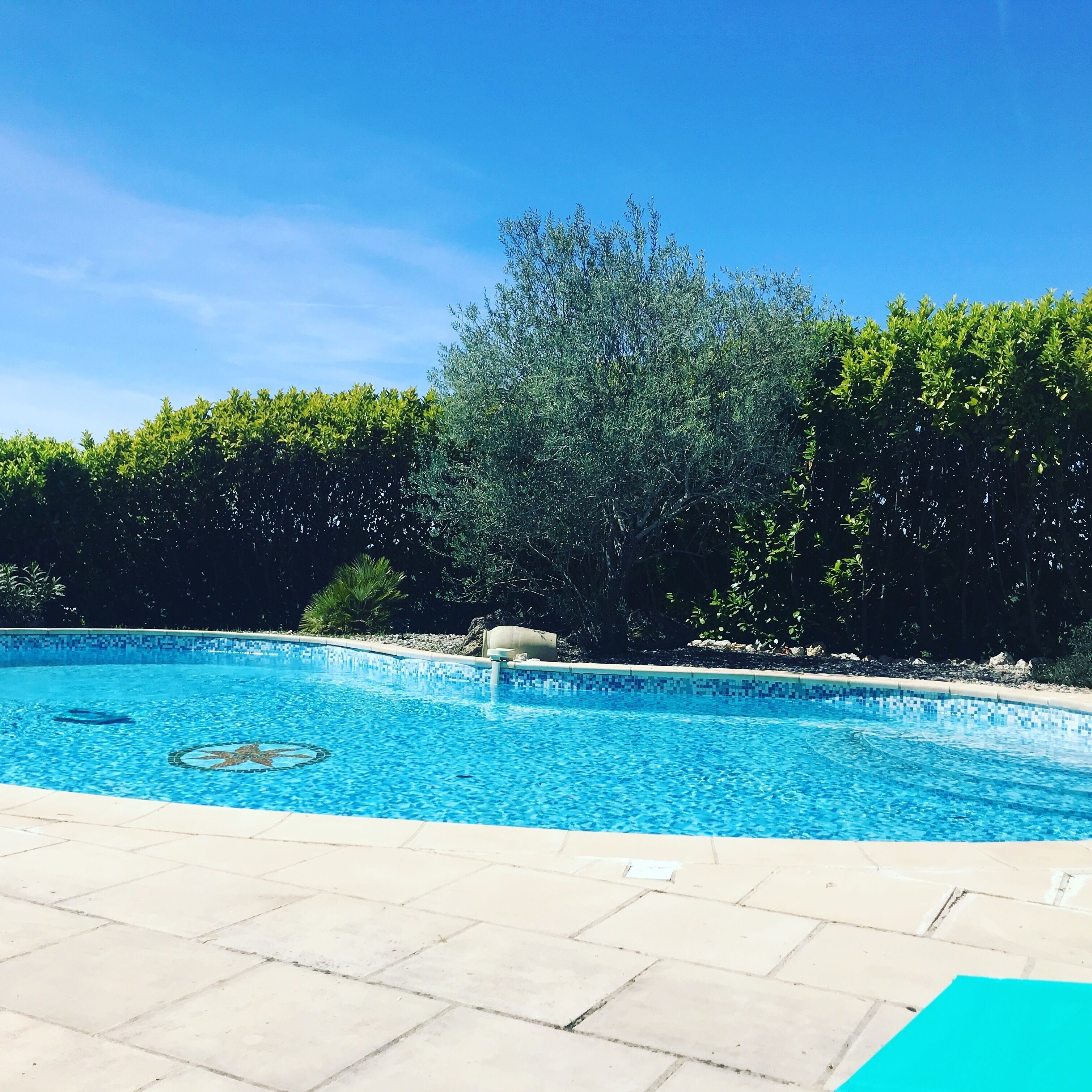 A clear blue swimming pool with a tiled edge, surrounded by a tiled deck area.