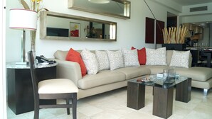 A modern living room with a beige sofa, patterned cushions, a glass coffee table, and a side table with a lamp. - Súper Condo 3 at Vidanta (Nuevo Vallarta)