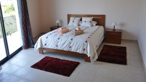 A bedroom with a bed, two nightstands, a red rug, and a view of greenery outside.