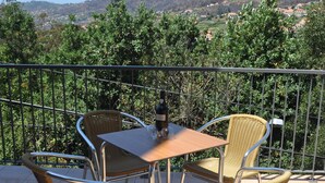 A balcony with a table and chairs, a bottle of wine, and a view of a hilly landscape.
