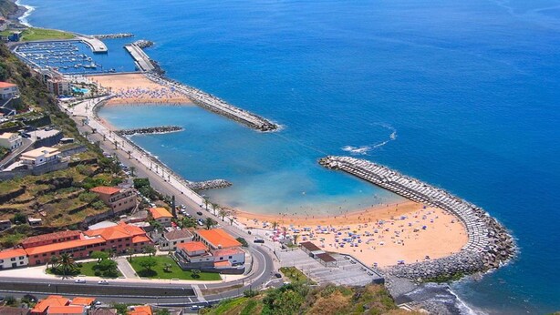 An aerial view of a coastal town with a beach, a curved breakwater, and a marina.