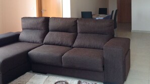 A living room with a sectional sofa, a dining table with chairs, and a door leading to another room.