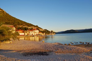 A coastal area with buildings along the shore, a sandy beach, and a calm body of water.