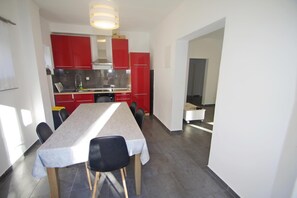 A modern kitchen with red cabinets, a stainless steel range hood, and a dining area with a table and chairs.