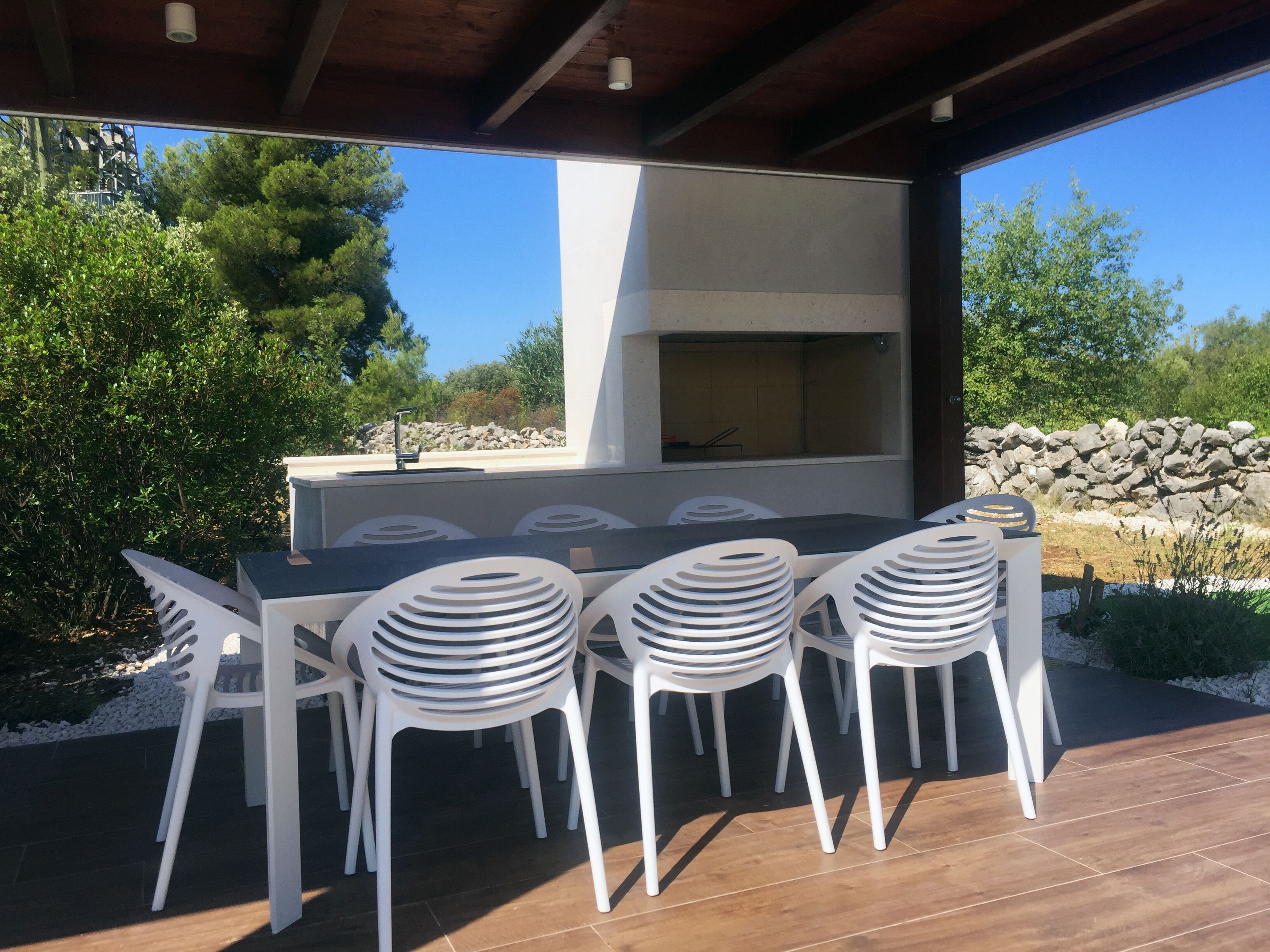 An outdoor patio with a built-in grill and white plastic chairs.