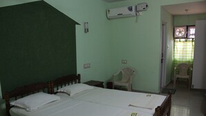 Ein Zimmer mit zwei Betten, einem Holzkopfende, einer Klimaanlage, einem Sessel und einem Fenster mit Vorhang.