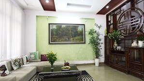 A living room with a sofa, a coffee table, a painting, and a cabinet with decorative items. - Hanoi Friendly House - Superior room - Queensize Bed (Hà Nội)