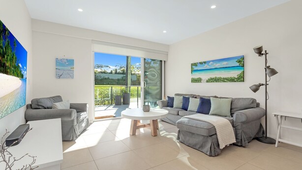 A modern living room with a grey sofa, a coffee table, and a balcony with a glass door. - Le Maison at the Beach (Huskisson)
