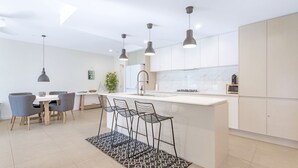 A modern kitchen with a central island, pendant lights, and bar stools. - Le Maison at the Beach (Huskisson)