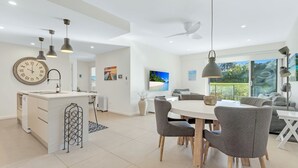 A modern kitchen with a central island, pendant lighting, and a large wall clock. - Le Maison at the Beach (Huskisson)
