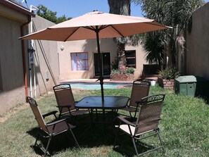Eine Terrasse mit Tisch und Stühlen, einem Sonnenschirm, einem Schwimmbad und einem Haus im Hintergrund.