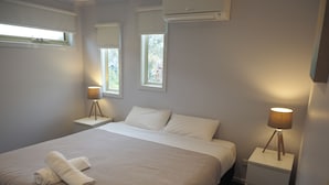 A neatly made bed with a folded towel, a bedside lamp, and a nightstand with a lamp. - The Beachcomber , Linen Supplied, 10 minute Walk to Surf Beach (Inverloch)