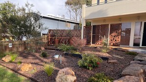 A landscaped garden with a variety of plants, rocks, and a metal fence. - The Beachcomber , Linen Supplied, 10 minute Walk to Surf Beach (Inverloch)