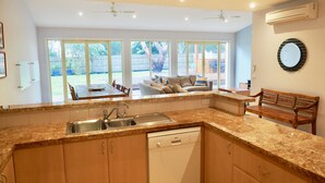 A modern kitchen with granite countertops, wooden cabinets, a Bosch dishwasher, and a dining area with a table and chairs. - The Beachcomber , Linen Supplied, 10 minute Walk to Surf Beach (Inverloch)