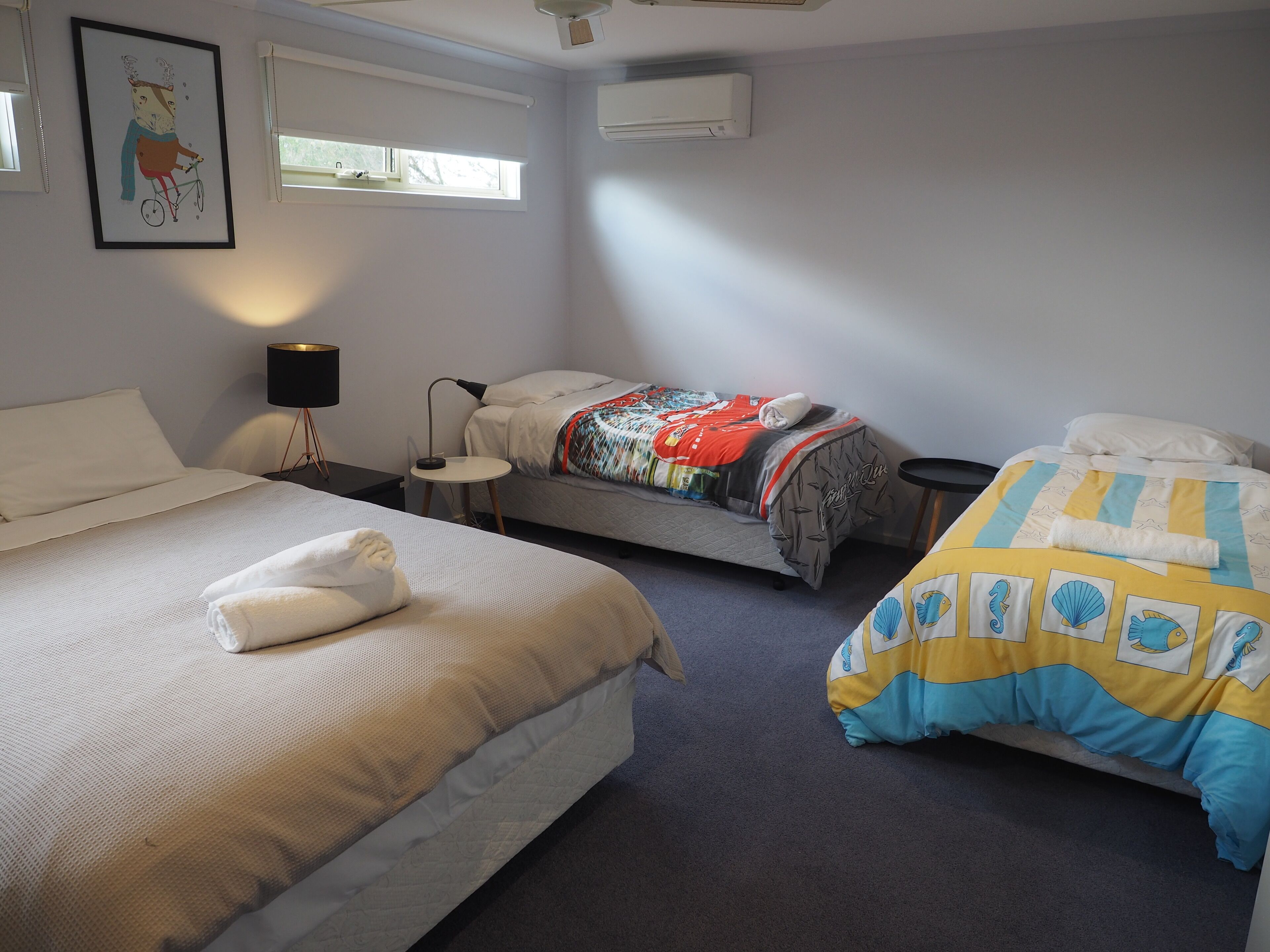 Une chambre d’hôtel avec deux lits, une petite table avec une lampe et un tableau encadré au mur.