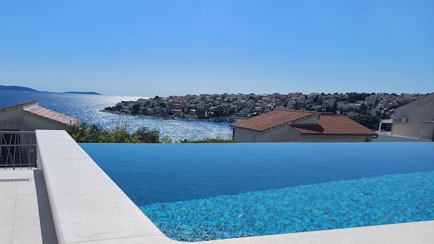 A swimming pool with clear blue water, surrounded by buildings and a view of the sea. - Heated swimming pool, spacious apartment with bay sea view terrace  ap3 (Okrug Gornji)
