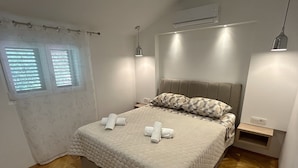 A neatly made bed with a headboard, a bedside table, and a window with blinds. - Heated swimming pool, spacious apartment with bay sea view terrace  ap3 (Okrug Gornji)
