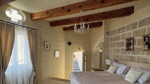 A bedroom with a large bed, a chandelier, stone walls, and a view of a staircase. - Cosy fully renovated farmhouse in Gozo (Xewkija , Gozo)