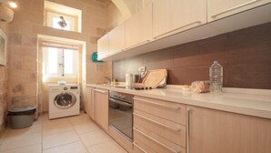 A compact kitchen with a washing machine, oven, and a countertop with a water bottle and bread. - Cosy fully renovated farmhouse in Gozo (Xewkija , Gozo)