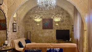 A room with a stone arch, a chandelier, a sofa, a TV, and a dining table with chairs. - Cosy fully renovated farmhouse in Gozo (Xewkija , Gozo)