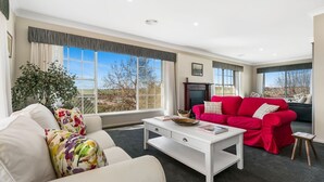 A modern living room with a white sofa, a red sofa, and a coffee table. There is a large window with curtains, a plant, and a fireplace.