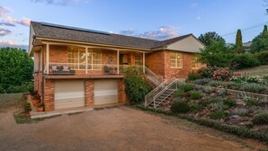 A two-story brick house with a covered porch, a garage, and a landscaped garden with various plants and flowers.